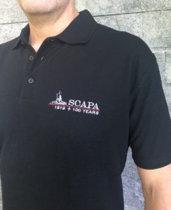 The Scapa Flow Centenary Polos are available in black and dark navy in S, M, L, XL, and XXL. They are made by in Orkney and can be ordered directly from John Kemp in Kirkwall or online. 